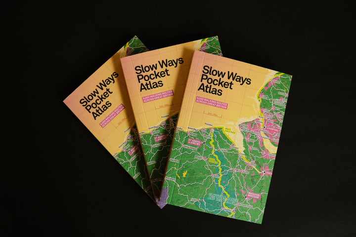 Three copies of the Slow Ways Pocket Atlas fanned out, showing their colourful Great Britain walking map covers.
